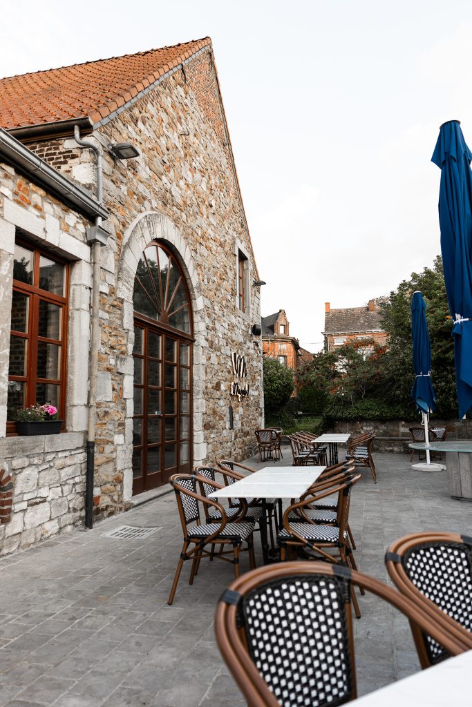 La terrasse de Magari, au pied de la façade en pierre, parasols bleus